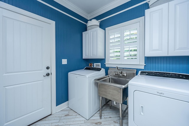 laundry room featuring crown molding, cabinet space, separate washer and dryer, a sink, and light wood-style flooring