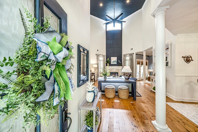 foyer with crown molding, ornate columns, a warm lit fireplace, and hardwood / wood-style floors