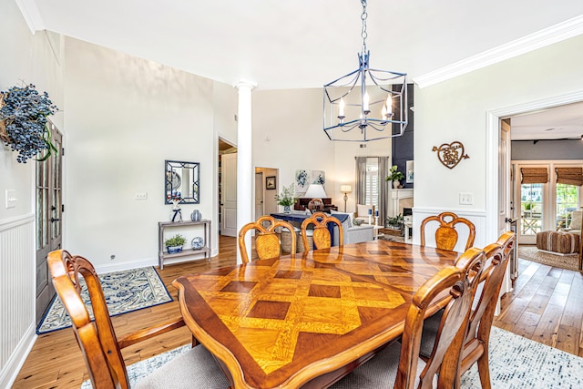 dining room with an inviting chandelier, a wainscoted wall, ornamental molding, and light wood-style flooring