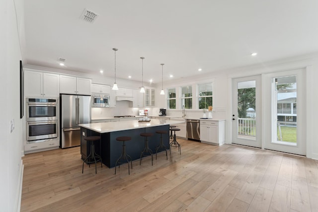 kitchen featuring a kitchen island, a kitchen bar, white cabinetry, appliances with stainless steel finishes, and ornamental molding