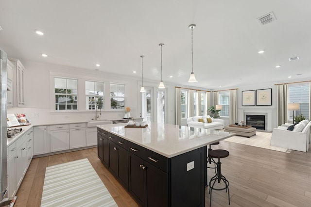 kitchen with decorative light fixtures, a kitchen island, sink, white cabinetry, and light hardwood / wood-style flooring