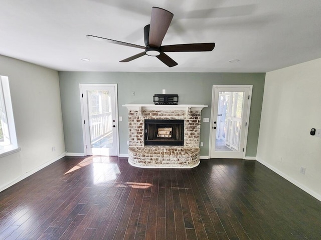 unfurnished living room featuring ceiling fan, plenty of natural light, dark hardwood / wood-style floors, and a brick fireplace