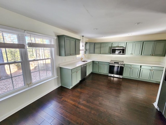 kitchen with appliances with stainless steel finishes, dark wood-type flooring, sink, pendant lighting, and green cabinetry