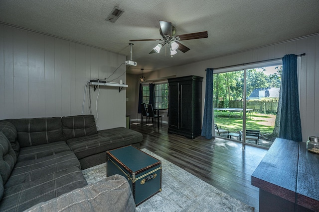 living room featuring ceiling fan, dark hardwood / wood-style flooring, a textured ceiling, and wooden walls