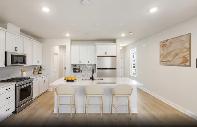 kitchen with white cabinets, an island with sink, stainless steel appliances, and backsplash