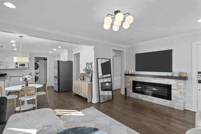 living room featuring a stone fireplace, dark hardwood / wood-style flooring, ornamental molding, and stacked washer and dryer