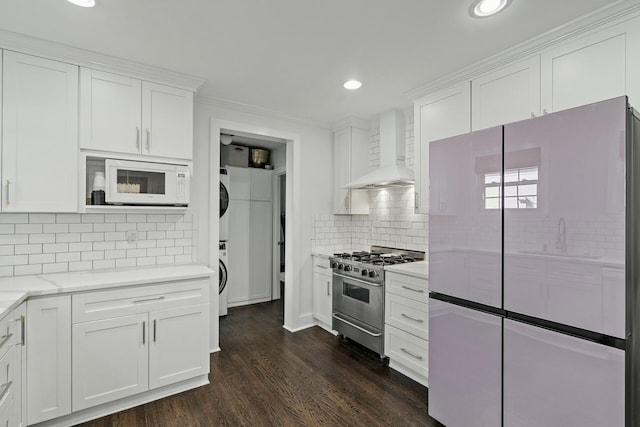 kitchen with white cabinetry, wall chimney range hood, white appliances, and stacked washer and dryer