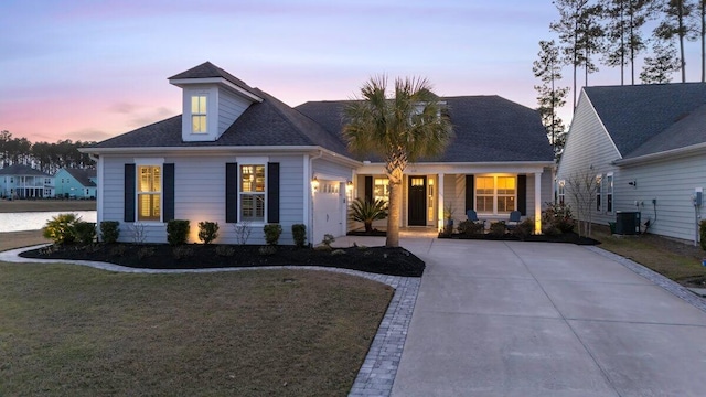 view of front facade with a shingled roof, a front yard, concrete driveway, and central AC