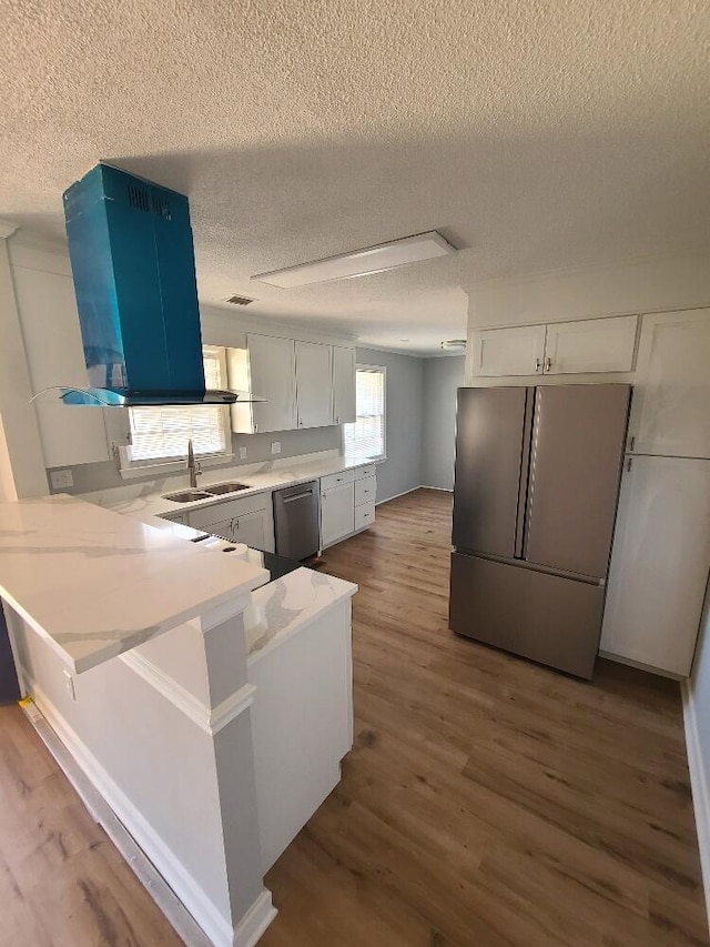 kitchen with a peninsula, wood finished floors, a sink, stainless steel dishwasher, and freestanding refrigerator