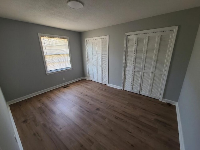 unfurnished bedroom with a textured ceiling, wood finished floors, two closets, and baseboards