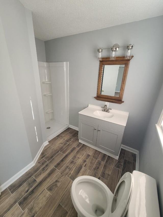 bathroom with a textured ceiling, wood finish floors, vanity, baseboards, and walk in shower