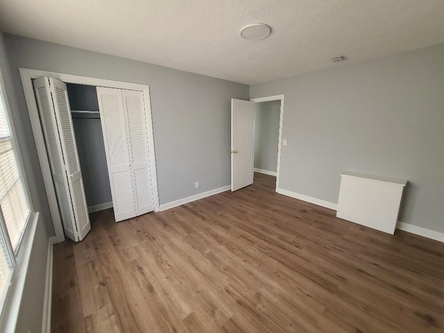 unfurnished bedroom with a textured ceiling, a closet, baseboards, and wood finished floors