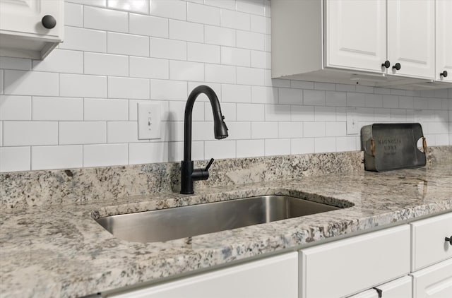 kitchen with white cabinetry, light stone countertops, backsplash, and a sink