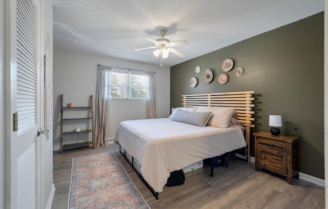 bedroom with a ceiling fan, wood finished floors, baseboards, and a textured ceiling