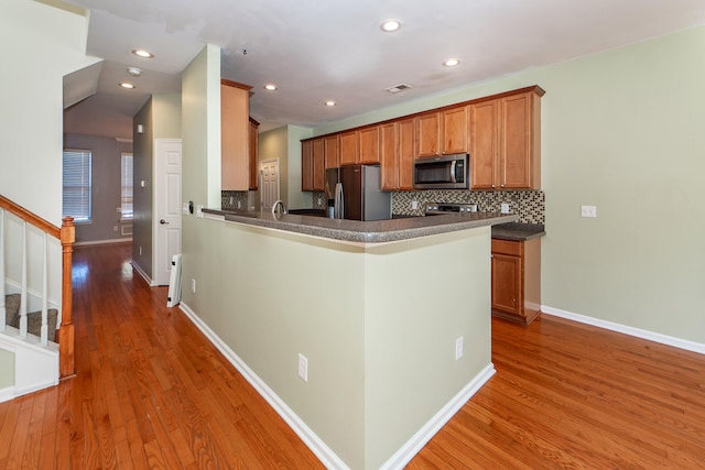 kitchen with decorative backsplash, dark hardwood / wood-style flooring, kitchen peninsula, and stainless steel appliances