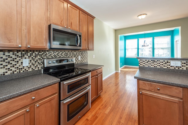 kitchen featuring backsplash, pendant lighting, light wood-type flooring, and appliances with stainless steel finishes