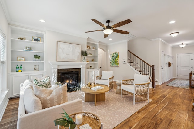 living room featuring hardwood / wood-style flooring, built in shelves, ceiling fan, crown molding, and a fireplace