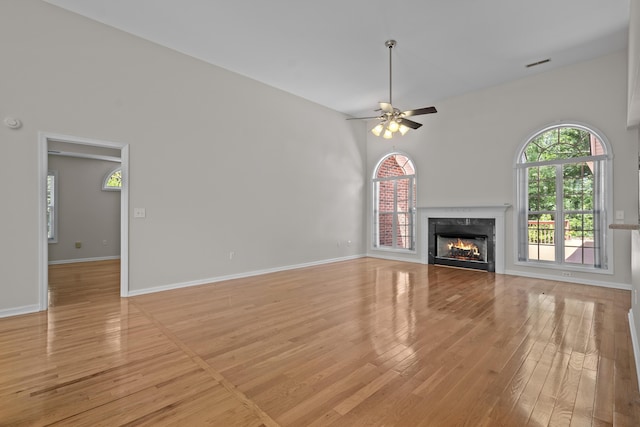 unfurnished living room featuring light wood-type flooring, a fireplace, a ceiling fan, baseboards, and a towering ceiling