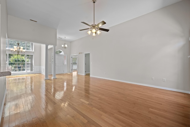 unfurnished living room with a chandelier, high vaulted ceiling, light wood finished floors, decorative columns, and a ceiling fan