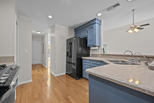 kitchen with a sink, black fridge, blue cabinetry, stainless steel gas range oven, and recessed lighting