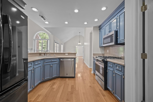 kitchen with appliances with stainless steel finishes, blue cabinetry, light wood finished floors, a peninsula, and light countertops