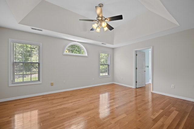 spare room with light wood-type flooring, a tray ceiling, ceiling fan, and baseboards