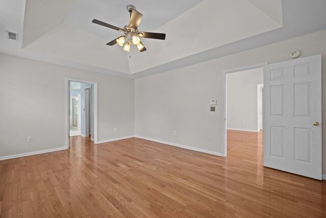 spare room featuring a tray ceiling, a ceiling fan, light wood-style floors, and baseboards