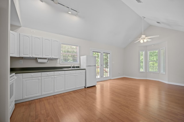 kitchen with white appliances, vaulted ceiling, track lighting, a sink, and dark countertops