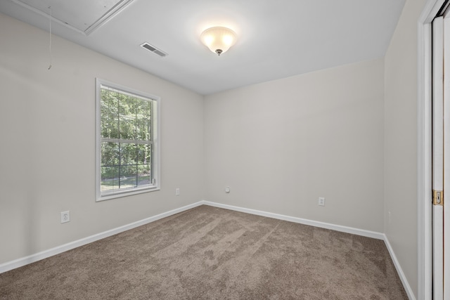 carpeted empty room with attic access and baseboards