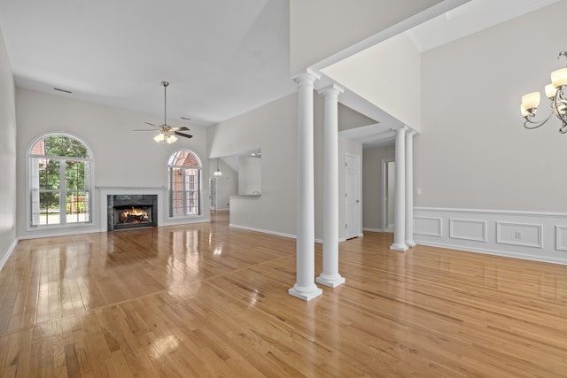 unfurnished living room with ceiling fan, a tile fireplace, light wood-type flooring, ornate columns, and high vaulted ceiling