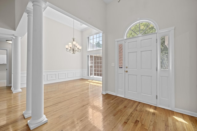 entrance foyer with ornate columns, high vaulted ceiling, light wood-style flooring, and a chandelier