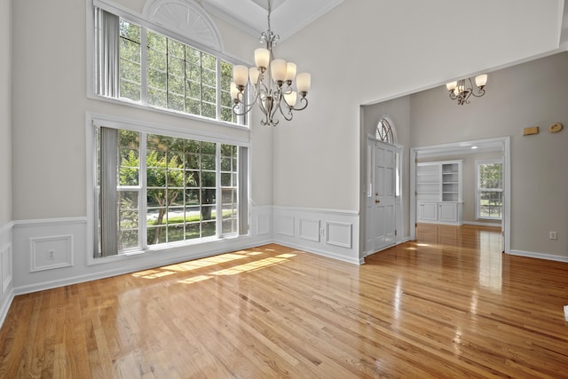 unfurnished dining area with a chandelier, wood finished floors, a wainscoted wall, a towering ceiling, and a decorative wall