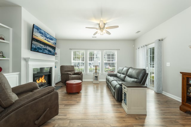 living room featuring built in shelves, ceiling fan, and light hardwood / wood-style flooring