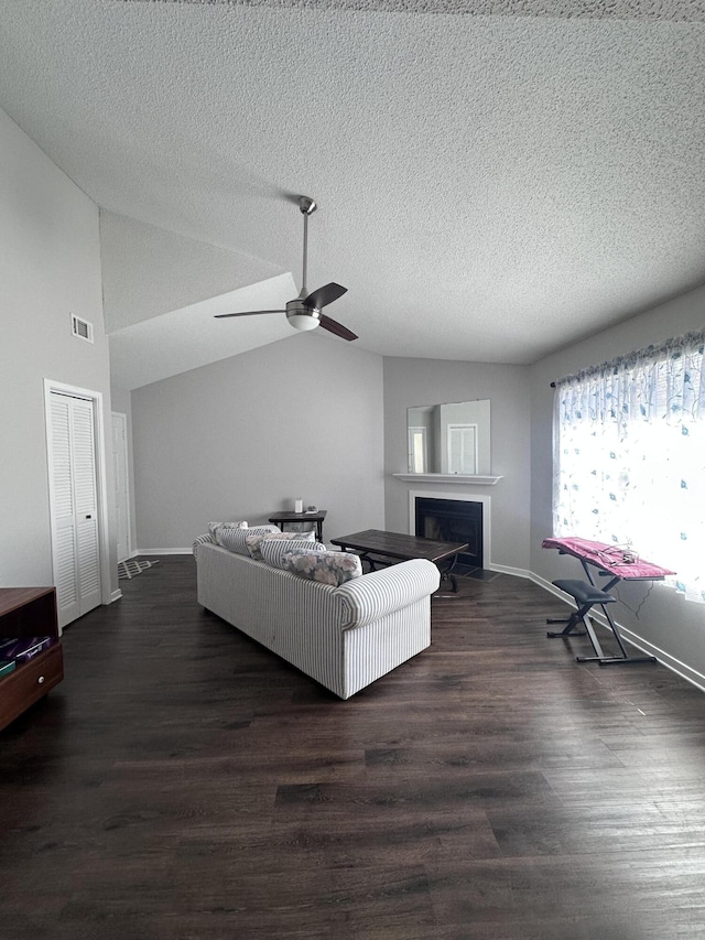 living room with a textured ceiling, lofted ceiling, a fireplace, visible vents, and dark wood-style floors