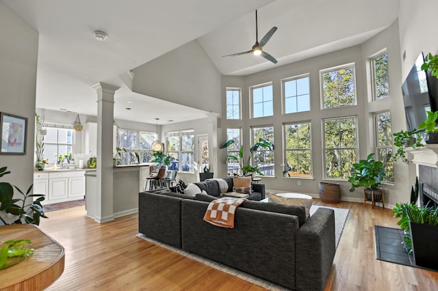 living room with decorative columns, light wood-type flooring, sink, a high ceiling, and ceiling fan