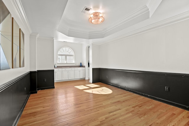 spare room featuring light hardwood / wood-style floors, a tray ceiling, and ornamental molding