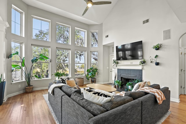 living room featuring light hardwood / wood-style floors, a high ceiling, a tile fireplace, and ceiling fan