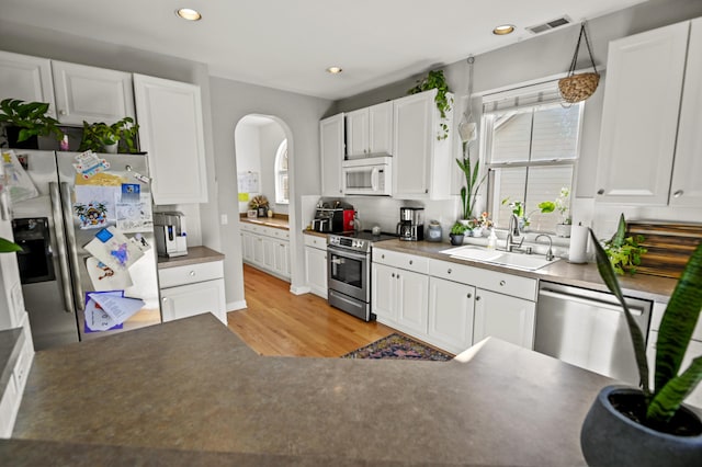 kitchen with light hardwood / wood-style floors, white cabinetry, hanging light fixtures, sink, and stainless steel appliances