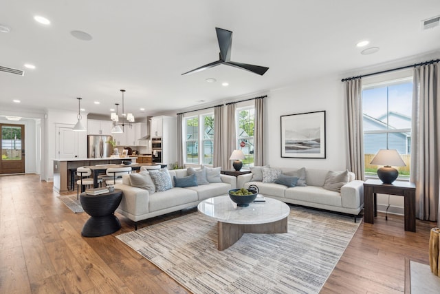 living room featuring light hardwood / wood-style floors, ceiling fan with notable chandelier, and plenty of natural light