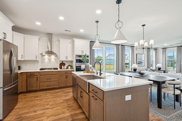 kitchen featuring stainless steel appliances, a kitchen island with sink, wall chimney range hood, pendant lighting, and white cabinets