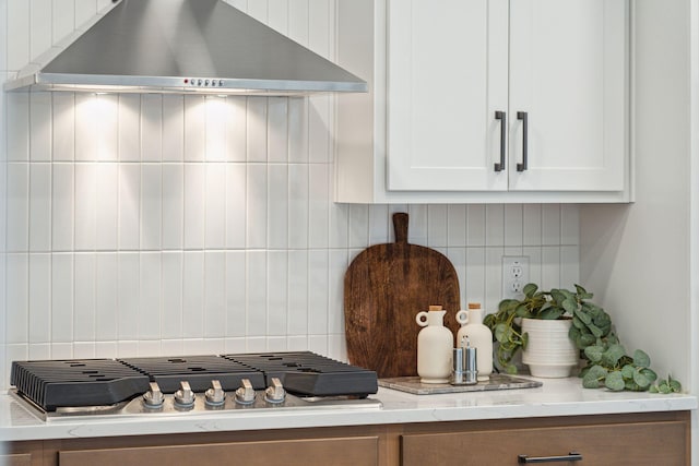 interior space with light stone countertops, white cabinets, wall chimney range hood, tasteful backsplash, and stainless steel gas cooktop