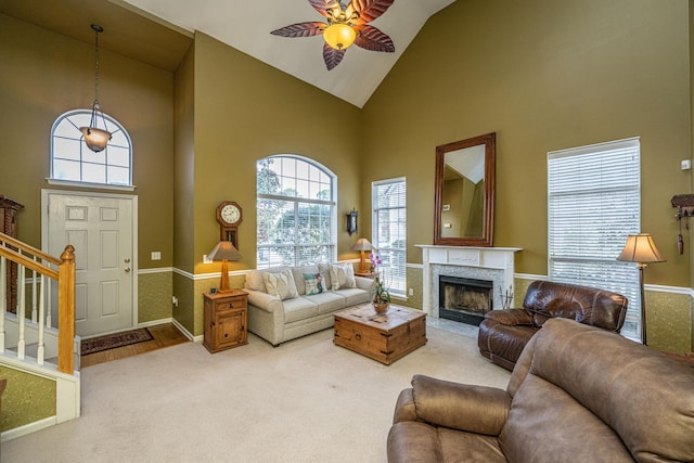 living room with a ceiling fan, a premium fireplace, stairs, carpet flooring, and high vaulted ceiling