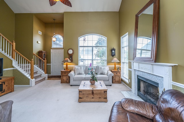 living room with a towering ceiling, ceiling fan, stairway, carpet, and a fireplace