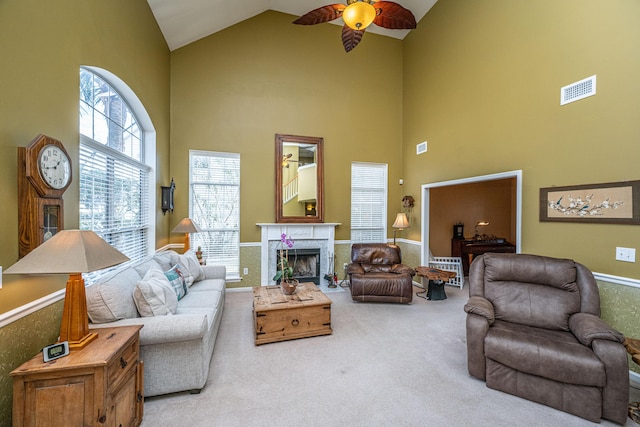 carpeted living room with high vaulted ceiling, ceiling fan, a fireplace, and visible vents