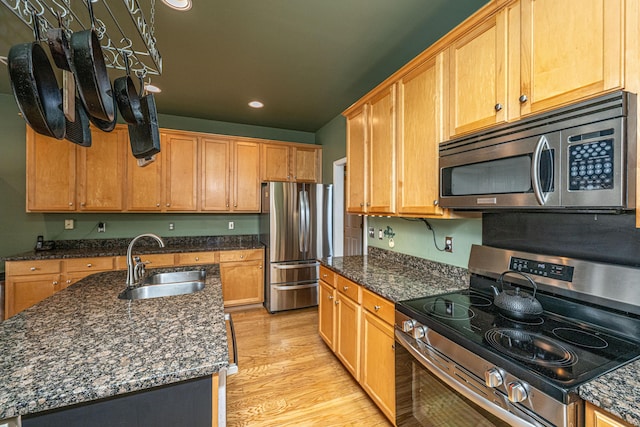 kitchen with recessed lighting, stainless steel appliances, a sink, light wood-type flooring, and dark stone counters