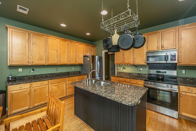 kitchen featuring visible vents, appliances with stainless steel finishes, a kitchen island with sink, light wood-style floors, and a sink