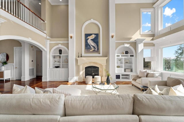 living room with plenty of natural light, built in features, wood finished floors, and a glass covered fireplace