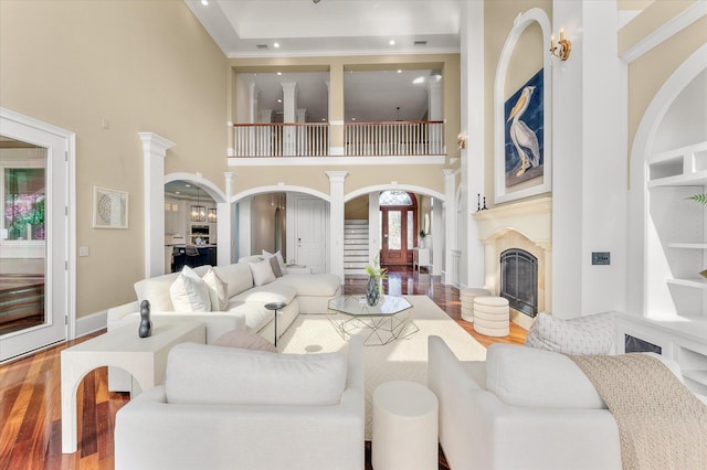 living room with crown molding, arched walkways, a fireplace, and wood finished floors