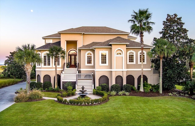 view of front facade featuring driveway, a front lawn, stairway, and stucco siding