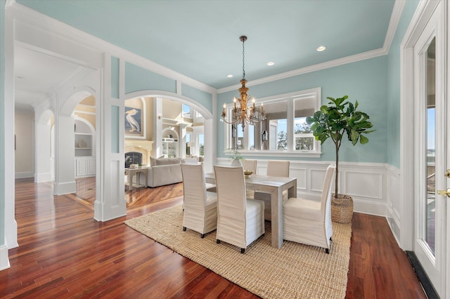 dining area with dark wood-style floors, arched walkways, a glass covered fireplace, and a decorative wall